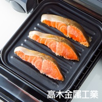 日本製烤箱用黑色波浪長盤，上面放有三塊未烹調的鮭魚排，鮭魚呈現鮮豔的橙紅色，帶有魚皮。