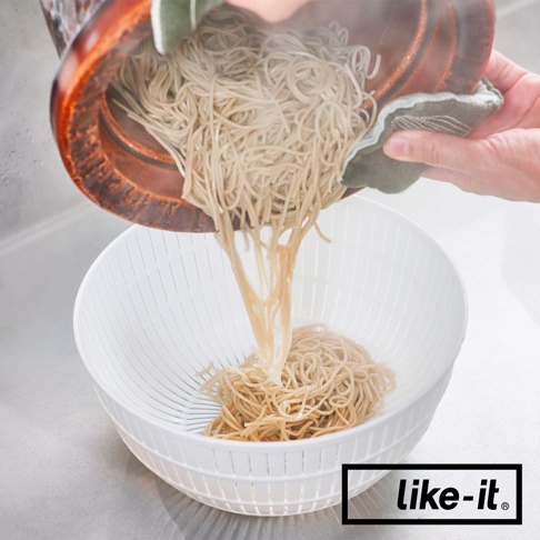 一個白色雙層塑膠瀝水籃，正在從一個木製容器中瀝乾蕎麥麵。