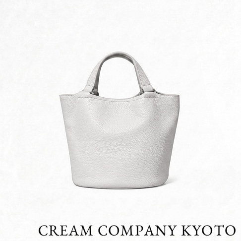 一個由 CREAM COMPANY KYOTO 品牌推出的白色皮革水桶托特包，包身採用質感細膩的 glove 牛皮革製作，外型小巧簡約，具備輕量耐用的特性，適合日常外出或隨身攜帶。
