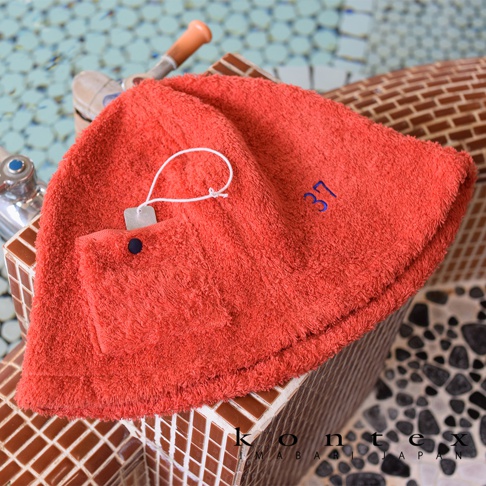 珊瑚橘色毛巾質料的桑拿帽，帽子上有藍色數字「37」刺繡，並有一個附有黑色鈕扣的毛巾質料小口袋。