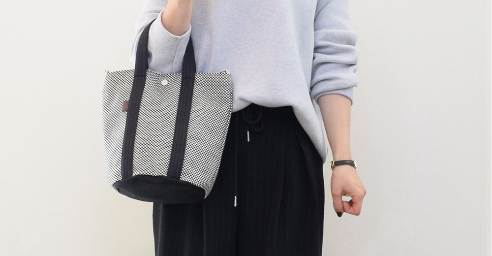 三河木綿刺子織兩用水桶包，白色格紋搭配黑色提把與底部，質感簡約，適合日常搭配。