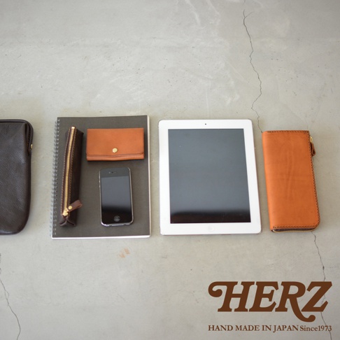 職人手作皮革Organ手拿包 G-38，包含深棕色皮革長夾、棕色皮革短夾、黑色手機、白色平板電腦，以及一本筆記本，皆以簡約的佈局呈現。