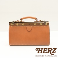 職人手作皮革復古口金兩用手提包，採用鞣製皮革製成，呈現溫潤的棕色調。包身結構紮實，配有金屬口金、黃銅色卯釘及提把，散發復古質感。包款線條簡潔，適合日常攜帶。