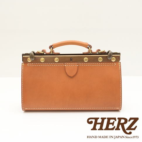 職人手作皮革復古口金兩用手提包，採用鞣製皮革製成，呈現溫潤的棕色調。包身結構紮實，配有金屬口金、黃銅色卯釘及提把，散發復古質感。包款線條簡潔，適合日常攜帶。