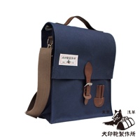 深藍色純棉帆布製成的直式側背包，配有棕色皮革提把、可調式斜背包帶，以及一個帶有金屬扣環的皮革翻蓋。