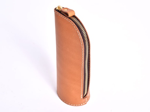 棕色皮革製成的直立式筆袋，側邊有黃銅拉鍊和米色縫線，頂部有皮革拉環。