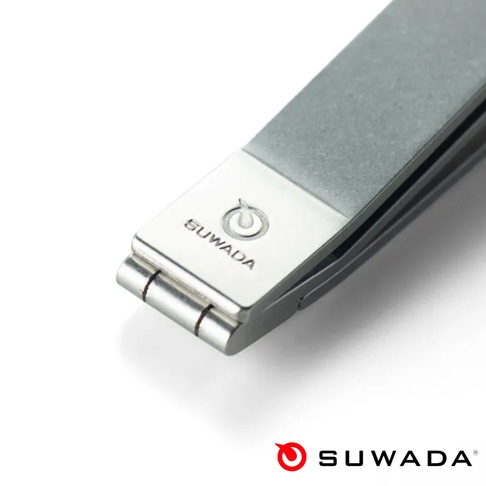 這張特寫照片展示了 SUWADA 諏訪田製作所的迷你款指甲剪，機身表面呈現帶有紋理的金屬質感。鏡頭聚焦在指甲剪的轉軸與品牌標誌處，上方刻有精緻的 SUWADA 商標，整體設計簡約現代，展現出日本職人工藝的精細品質。