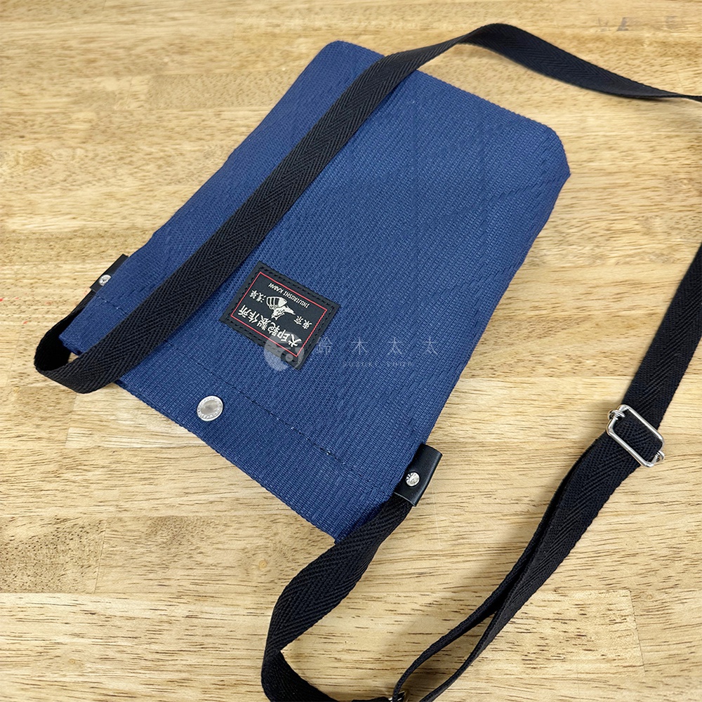 深藍色刺子織平板收納側背包，有黑色織帶肩帶，上面印有「大印記製作所」字樣的黑色標籤。