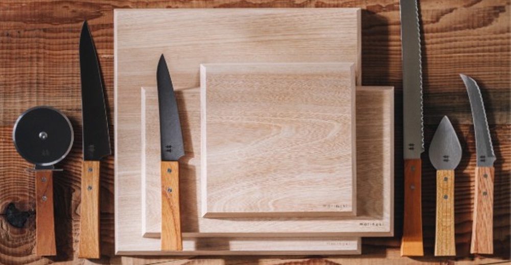 多款 morinoki 榆木砧板與志津匠黑色刀具，包含披薩輪刀、主廚刀、麵包刀、起司刀及切片刀，擺放在木紋背景上。