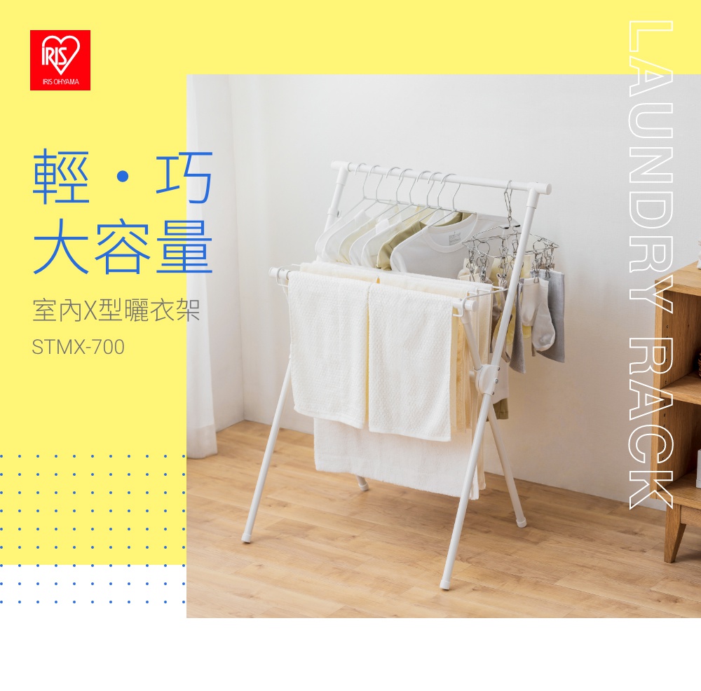 白色金屬材質的室內X型曬衣架，上方掛有衣架及衣物，下方層架上疊放著白色毛巾，整體設計簡潔實用。