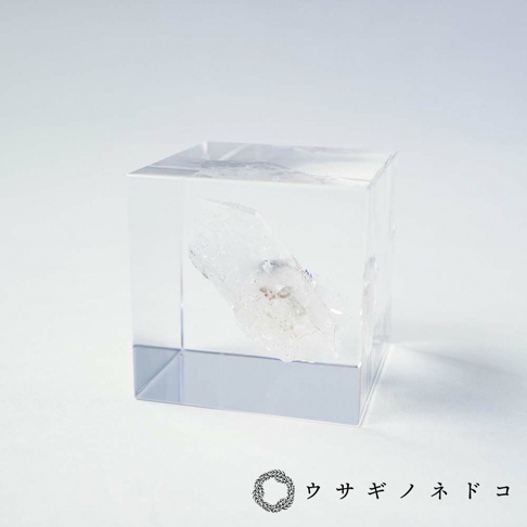 透明立方體壓克力中封存著一塊天然白水晶，水晶呈現半透明狀，內部帶有細微雜質與紋理，整體色調為白色與透明。