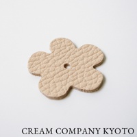 淺米色皮革製成的五瓣花形小吊飾，表面壓有細緻紋路，中央有一個小孔，適合搭配京都職人手作手提托特包。