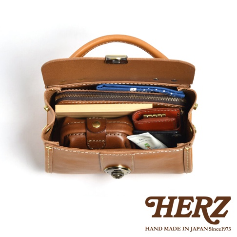 職人手作皮革迷你手提包，標誌性焦糖色皮革，設計簡約，內有隔層，可收納鑰匙包、小錢包、化妝品和紙製品。包款上方配有提把，前方設有金屬鎖扣，整體風格經典復古。