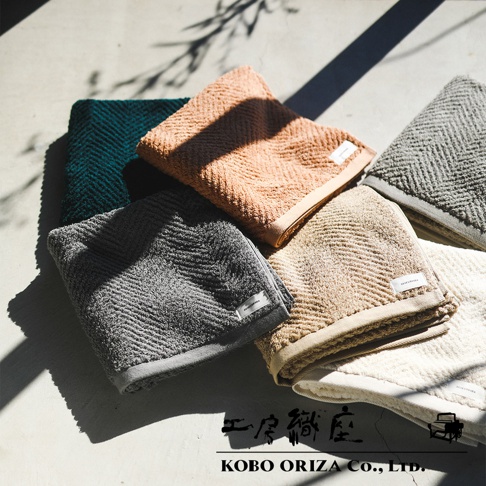 五條不同顏色的有機棉毛巾，呈現人字紋織法，包括深綠、橘粉、淺灰、米白及卡其色。