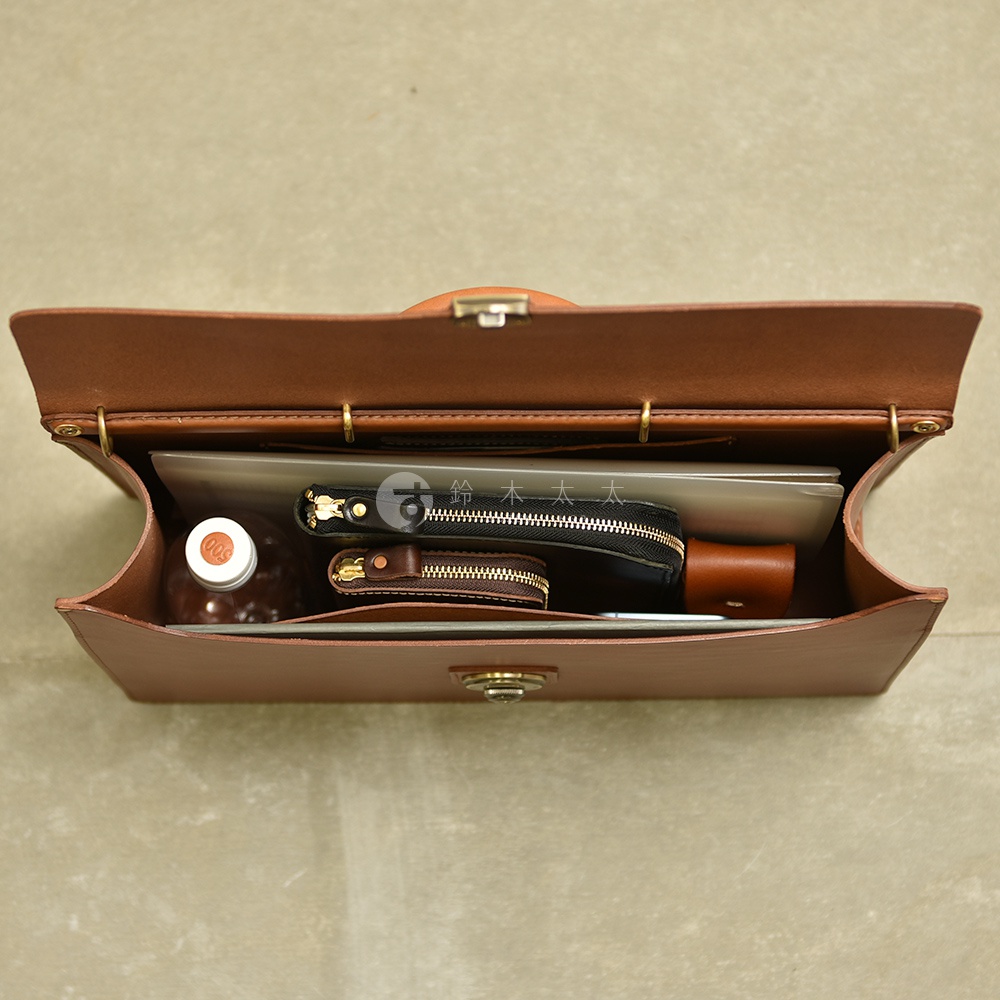 職人手作皮革Organ兩用商務公事包，展現精緻皮革紋理，內部整齊收納平板電腦、筆記本、拉鍊錢包、零錢包及一瓶飲料，設計簡約實用。