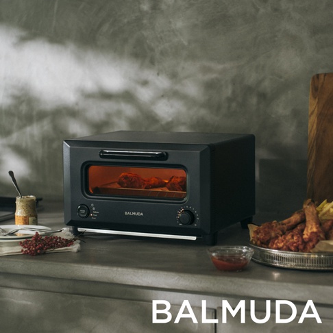 黑色 BALMUDA 烤麵包機，內部有烤雞腿，側面有炸雞和薯條，以及一碗醬料。
