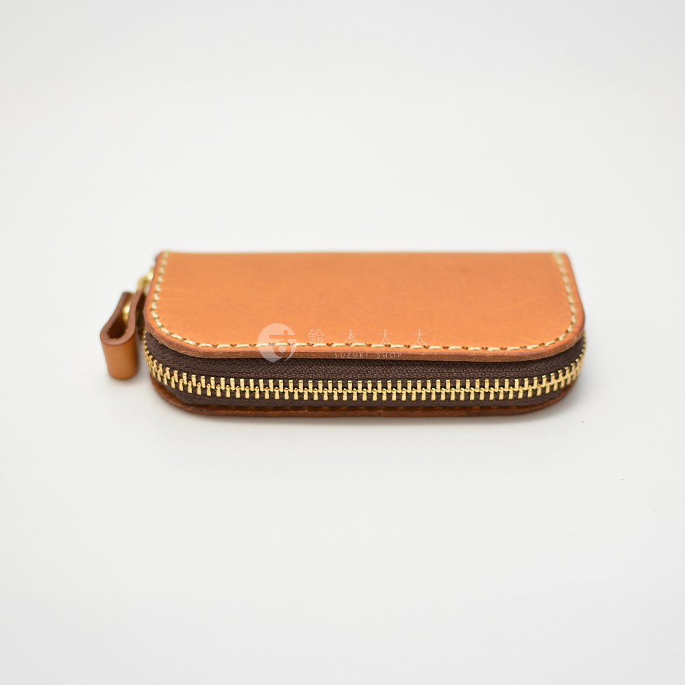 職人手作皮革橢圓形拉鍊鑰匙包，咖啡色皮革搭配棕色車縫線和金色拉鍊，左側附有皮革拉環。