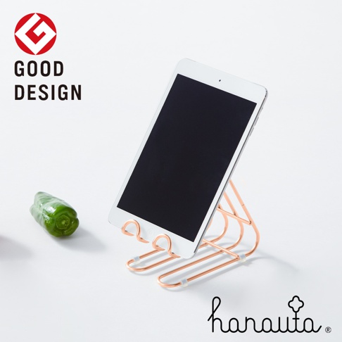 一個玫瑰金色不鏽鋼萬用支架，上面放置著一部平板電腦，左側有一個綠色甜椒。