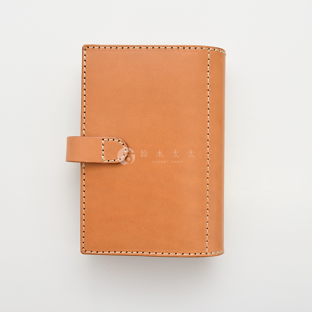淺棕色皮革手帳，側面有縫線裝飾，前方有皮革束帶扣。
