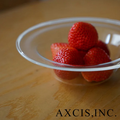 一個透明玻璃製成的深型點心碗，裡面盛有幾顆鮮紅色的草莓，碗放在木質桌面上。