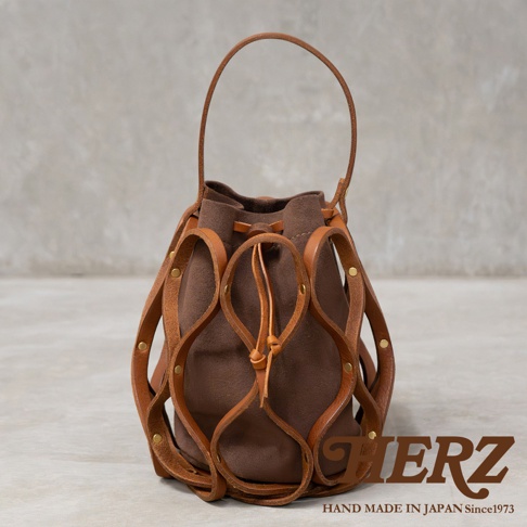 日本HERZ職人手作皮革Organ編織水桶包 G-98，採用咖啡色麂皮內袋與棕色皮革編織網格外層，搭配皮革提把，底部有金屬腳釘，右下角有HERZ品牌標誌及HAND MADE IN JAPAN Since1973字樣。