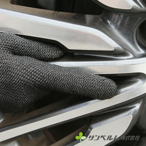一隻黑色網狀紋理的清潔手套，手指部分正接觸汽車輪框的銀色與黑色凹槽細節。
