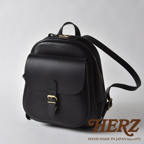 黑色皮革迷你後背包，設有立體前袋、黃銅釦環及拉鍊，背帶可調節，整體風格簡潔。