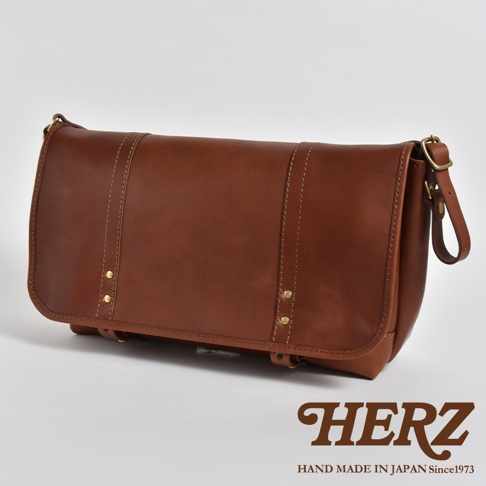 職人手作皮革復古郵差包，呈現深棕色調，以精緻縫線和金屬鉚釘裝飾，風格經典，適合日常攜帶。