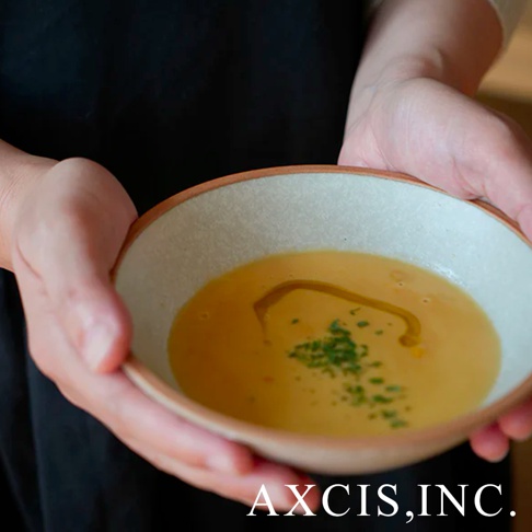 一雙手捧著一個素燒陶瓷沙拉碗，碗中盛有濃湯，表面淋上橄欖油並撒上香草碎，碗邊緣為樸實的陶土色。