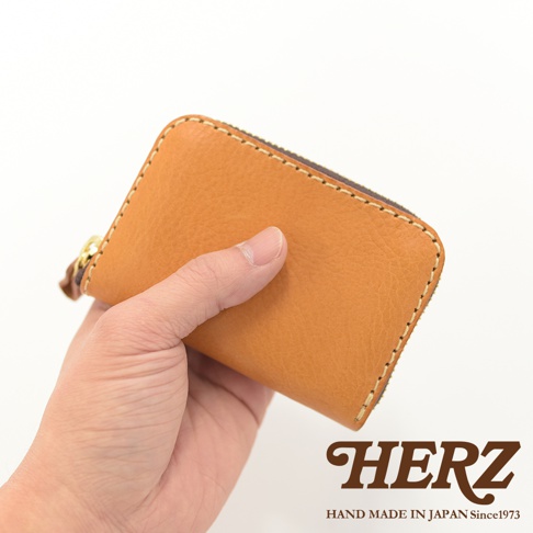 手持駱駝色皮革拉鍊零錢包，錢包表面有細緻紋路，搭配淺色車線及金色拉鍊。