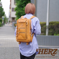 一位女士背著棕褐色皮革製成的兩用多功能後背包，背包上有兩個拉鍊隔層和一個頂部翻蓋口袋，側面有可調節的皮革帶。