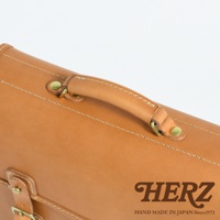 職人手作皮革商務休閒兩用單肩包，展示其光滑的棕褐色皮革表面、精緻的縫線細節、金屬扣環和皮質提把。