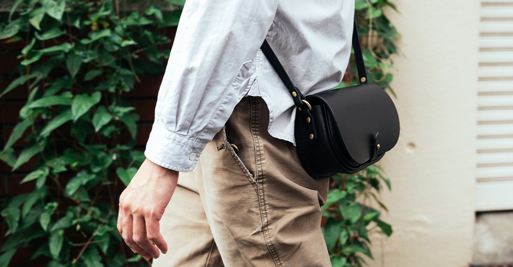 黑色皮革迷你馬鞍包，附有金色金屬扣件和可調式肩帶，由職人手工製作。