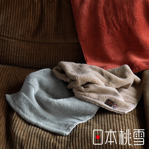 今治匹馬棉毛巾，展示了淡藍色、淺褐色和磚紅色。毛巾質地柔軟，堆疊在有紋理的布料背景上，其中一條淺褐色毛巾上帶有品牌標籤。