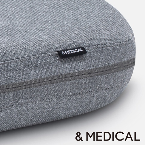 灰色紋理布料製成的圓形按摩指壓枕，帶有拉鍊和黑色標籤，上面印有白色 & MEDICAL 字樣。