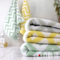 一疊三條今治毛巾，紋理為鋸齒狀，顏色有淺綠、黃白相間、灰白相間。另外兩條毛巾掛在背景牆上，顏色為淺綠與黃色。