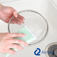 雙手拿著一個圓形金屬網籃，網籃上方有細緻的網格，網籃底部有泡沫。左手拿著綠色網格海綿，正在清潔網籃。