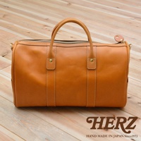 棕褐色皮革製成的職人手作波士頓包，具備雙提把、頂部拉鍊開合，以及側邊可掛肩帶的金屬扣環。包身縫線清晰，質感自然。