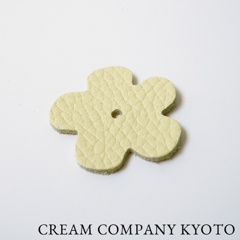 淡黃色皮革製成的四瓣花形吊飾，表面有細緻紋理，中央有一個小孔。