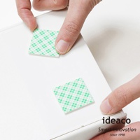 兩塊綠色格紋雙面膠帶被手指按壓在白色平面上，右下角印有「ideaco Smart Innovation Since 1998」字樣。