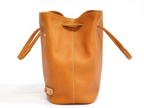 職人手作皮革可調式兩用大容量托特包，為棕褐色牛皮材質，束口設計，附有兩條可調整皮革提把，包體側面有縫線裝飾，底部有一個皮革製的固定扣。