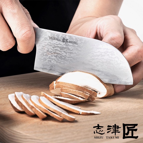 志津匠 Miyako 品牌廚刀正在切片香菇，刀刃呈現鍛造紋理，木質砧板上擺放著切好的香菇片。