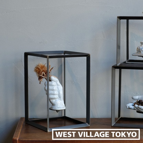 兩個黑色鐵製方形展示架，其中一個架子內有一個白色陶瓷手造型花器，手裡握著乾燥的植物裝飾。