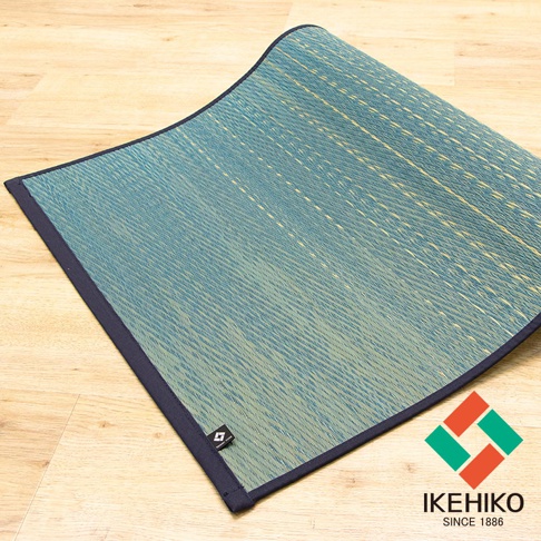 藺草編織的瑜珈墊，呈現藍綠色漸層，邊緣為深藍色滾邊，帶有止滑設計，質感樸實自然。