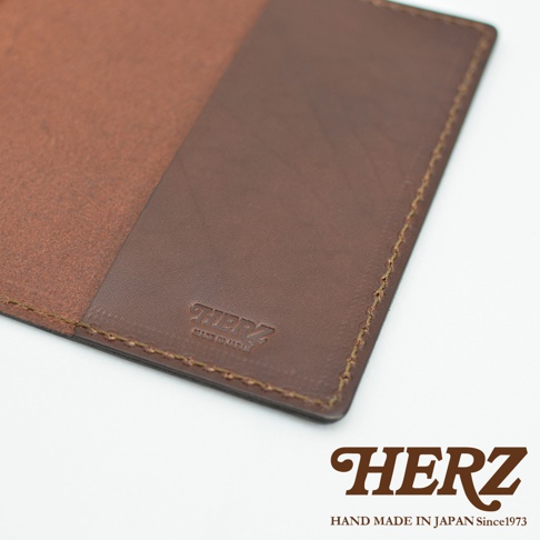 深棕色皮革護照套，內部有兩個隔層，其中一個隔層印有「HERZ」和「MADE IN JAPAN」字樣，周圍有縫線。