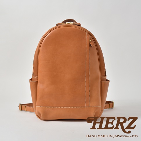 職人手作皮革多功能後背包 R-21，採用光滑的棕褐色皮革材質，設計簡潔，正面有垂直縫線和側邊口袋，整體呈現溫潤質感。