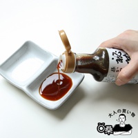 一隻手拿著塑膠瓶，將深棕色的秘藏豬排沾醬，倒進一個白色雙格小碟子裡。