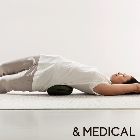 一名女子側躺在瑜珈墊上，使用一個綠色、U型、有紋路的骨盤枕支撐腰部。