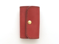 紅色皮革經典鑰匙包，配有六個鉤子和一個黃銅按扣，以咖啡色縫線手工製作，整體設計簡潔。