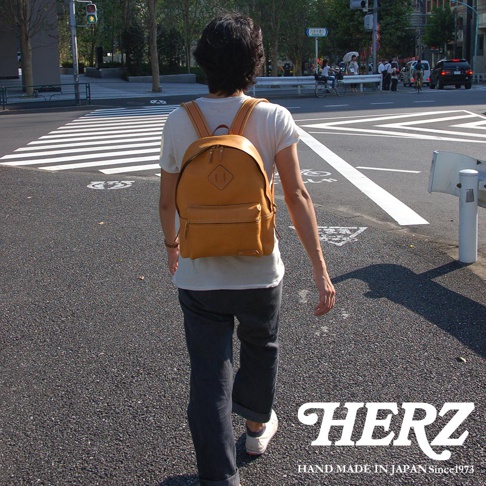 棕色皮革後背包，兩側有拉鍊口袋，正面有一個較小的拉鍊口袋，頂部有菱形皮革裝飾。